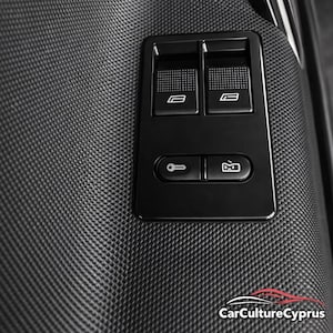 Könnte beinhalten: Nahaufnahme einer schwarzen Autotürverkleidung mit Fenster- und Türverriegelungsbedienelementen. Die Verkleidung hat ein strukturiertes Muster. Die Fensterbedienelemente haben ein Fenstersymbol.