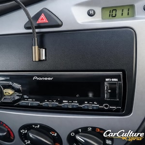 Może przedstawiać: Radio samochodowe Pioneer ze srebrnym panelem przednim i czarnymi przyciskami jest zainstalowane w desce rozdzielczej samochodu. Deska rozdzielcza jest szara i czarna, z cyfrowym zegarem wskazującym 10:11. Czarny kabel audio jest podłączony do radia.