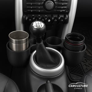 May include: Black car interior with a gear shift, cup holders, and a stainless steel tumbler. A black lens is in the other cup holder. The text "CARCULTURE CYPRUS" is visible.