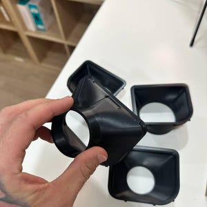 May include: A set of black, 3D-printed plastic funnel-shaped components with a square-to-round transition design. Each piece features a wide square opening that tapers down to a circular aperture, showcasing a smooth, matte finish and rigid construction.