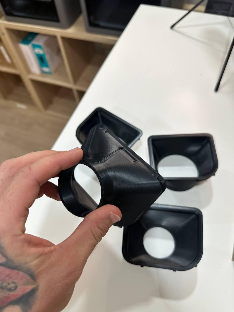 May include: A set of black, 3D-printed plastic funnel-shaped components with a square-to-round transition design. Each piece features a wide square opening that tapers down to a circular aperture, showcasing a smooth, matte finish and rigid construction.