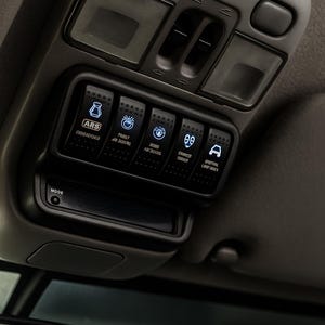 May include: A car's overhead console, showing illuminated switches and controls. The black and grey console has various labelled buttons for different vehicle functions. The image includes the text "ARS", "PROUT", "SAMPED", and "OPTINIL".