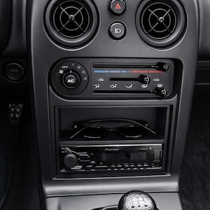 Puede incluir: Interior del salpicadero de un coche gris oscuro. Incluye rejillas de ventilación, controles de climatización y una radio Pioneer. Las gafas de sol descansan en un compartimento debajo. También se ve la palanca de cambios.