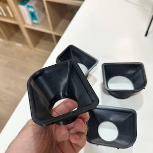 May include: A set of black, 3D-printed plastic funnel-shaped components with a square-to-round transition design. Each piece features a wide, square-shaped opening that tapers down into a circular aperture, showcasing a smooth, matte finish.