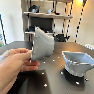 May include: Two light gray, 3D-printed plastic funnel-shaped components with a wide, square-edged opening that tapers down to a circular base. Each piece features small, evenly spaced rectangular tabs along the outer rim of the square opening.