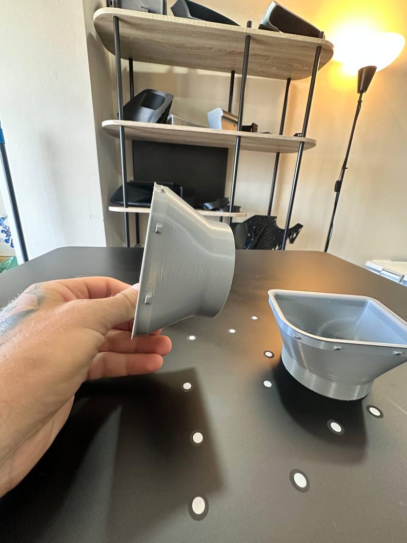 May include: Two light gray, 3D-printed plastic funnel-shaped components with a wide, square-edged opening that tapers down to a circular base. Each piece features small, evenly spaced rectangular tabs along the outer rim of the square opening.
