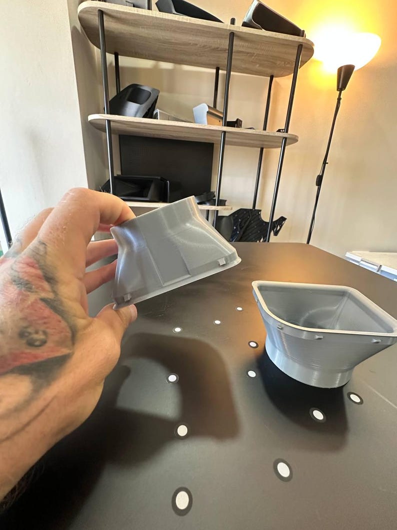 May include: Two light gray, 3D-printed plastic components with a flared, funnel-like shape. Each piece features a square opening at the top that tapers down to a circular base, with small, evenly spaced tabs protruding along the square rim edge.