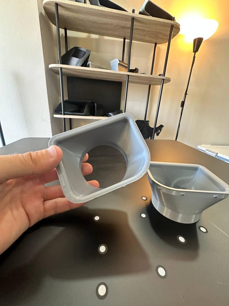 May include: Two grey, 3D-printed plastic funnel-shaped components with a square-to-round transition design. Each piece features a wide, square-shaped opening that tapers down into a circular aperture, showcasing visible layer lines from the manufacturing process.