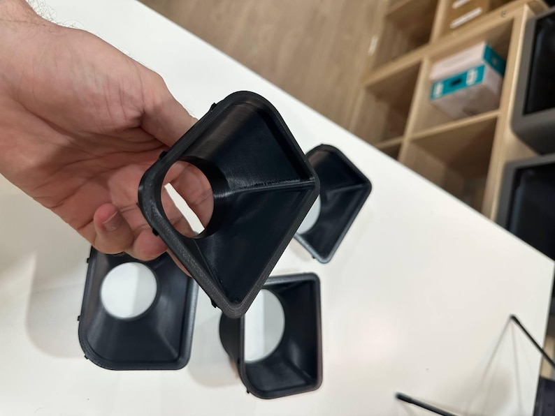 May include: A set of four black, funnel-shaped plastic components with a square outer rim and a circular inner opening. Each piece features a tapered design that narrows from the square frame toward the center hole, showing a smooth finish.