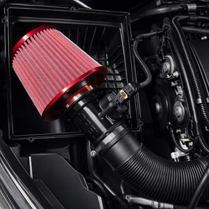 Könnte beinhalten: Eine rot-schwarze Kfz-Luftfilterbaugruppe, die in einem Motorraum eines Autos eingebaut ist. Der Filter hat ein rotes Maschenelement und ein schwarzes Gehäuse. Die Baugruppe umfasst ein schwarzes Ansaugrohr und verschiedene Motorkomponenten.