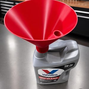 May include: A bright red plastic funnel is inserted into the spout of a gray plastic jug of Valvoline 5W-20 High Mileage synthetic motor oil. The jug features a white label with the Valvoline logo, text, and a red and blue chevron graphic.