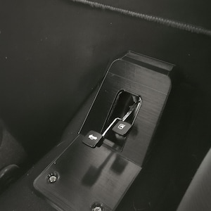 Könnte beinhalten: Schwarzes Autoinnenraumteil mit strukturierter Oberfläche. Verfügt über einen Hebel und Knöpfe mit Autosymbolen. Das Bauteil ist mit Schrauben befestigt. Das CarCulture.CYPRUS-Logo ist sichtbar.