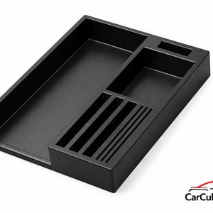 May include: A black car organizer with multiple compartments. It features a large rectangular tray, a smaller rectangular section, and a section with several vertical slots. The organizer is designed to keep items tidy.