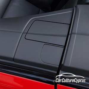 Pode incluir: Close-up do painel da porta interior de um carro. O painel é preto com acabamento fosco e apresenta compartimentos de armazenamento embutidos. A parte inferior da imagem mostra uma porta de carro vermelha. O texto "Car Culture Cyprus" é visível.
