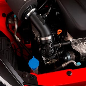 Può includere: Primo piano del vano motore di un'auto con un sistema di aspirazione dell'aria nero. Il filtro dell'aria ha la scritta "TWER". Il vano motore è rosso con vari componenti neri e fascette argentate.