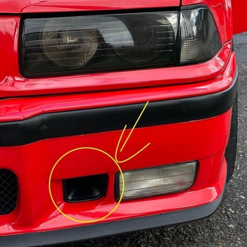 May include: A bright red car bumper featuring a black trim strip, a rectangular clear fog light, and a small black air intake duct highlighted by a yellow hand-drawn circle and arrow indicating the specific location of the cooling vent.