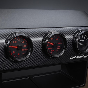 May include: A black dashboard with three gauges. The gauges have red illuminated needles and markings, displaying boost, oil pressure, and voltage readings. The dashboard has a carbon fibre texture.