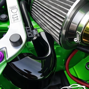 May include: Close-up of a car engine bay with a bright green finish. The image features a silver air filter, black intake tube, and various engine components. A silver strut bar with the text "13%" is also visible.