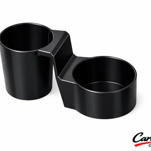 May include: A black dual cup holder featuring two cylindrical compartments connected by a central bridge. The unit has a smooth, matte finish and a rigid structure. The text CarCulture CYPRUS is printed in the bottom right corner of the image.