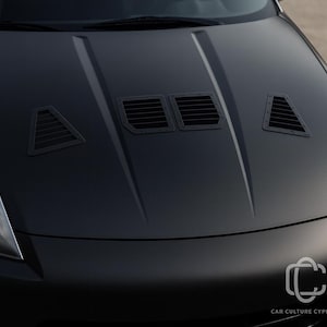 May include: Close-up of a matte black car bonnet featuring three black air vents. The bonnet has a smooth, curved design. The vents are rectangular and triangular, adding a sporty look. The car's front end is visible.