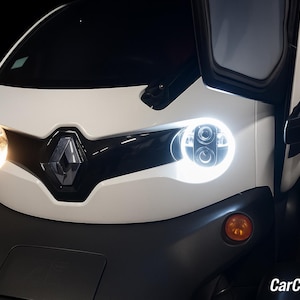 Peut inclure: Gros plan d'une voiture électrique blanche et grise avec le logo Renault à l'avant. La voiture a des phares lumineux et des feux de position orange. La portière de la voiture est ouverte.