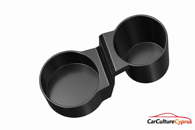 May include: A black dual cup holder with two circular openings connected by a central bridge. The object features a smooth, matte finish and a solid construction. In the bottom right corner, the text CarCultureCyprus appears in black and red.