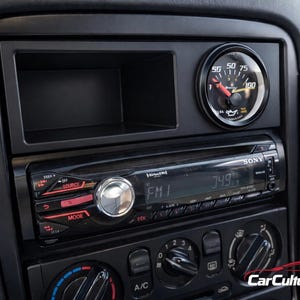 Puede incluir: Un salpicadero negro de coche con un equipo de música Sony, un indicador de presión de aceite y controles de aire acondicionado. La radio muestra "FM1" y "749". El indicador marca aproximadamente 75. El salpicadero es negro.