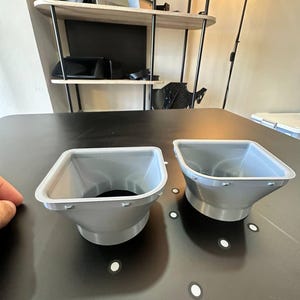 May include: Two light gray, funnel-shaped plastic components with a wide, square-like opening that tapers down to a circular base. Each piece features a flat, wide rim with small, evenly spaced protrusions along the outer edge of the top opening.