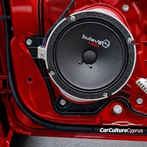 Puede incluir: Primer plano del interior de una puerta de coche roja brillante con un altavoz negro con la marca "BULAVA NEO" en blanco. Se ven cables y otros componentes. La imagen muestra detalles.