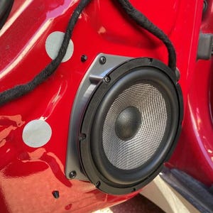 Peut inclure: Gros plan sur une portière de voiture avec un haut-parleur installé. Le haut-parleur est rond et possède une grille noire. La porte est rouge et un fil noir longe le côté.