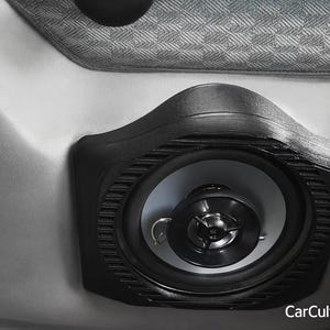 以下が含まれることがあります： 黒いプラスチック製のハウジングに取り付けられた円形の黒いカースピーカー。中央のツイーターとライトグレーのコーンが特徴です。スピーカーは滑らかなライトグレーの表面に配置され、上部にはテクスチャ加工されたグレーのファブリックパネルがあります。テキストはCarCultureCyprusと書かれています。