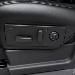 Puede incluir: Primer plano de un asiento de coche de cuero negro con controles integrados. El asiento cuenta con un panel de control con un interruptor basculante, un interruptor vertical y un dial circular. El asiento es parte del interior de un vehículo.