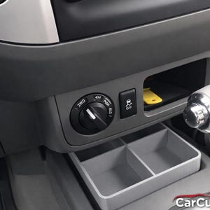 May include: Interior view of a car's dashboard, featuring a gray plastic console with a 4WD control knob, a storage compartment, and a divided tray. A yellow key is visible in the compartment. The gear shift is on the right.