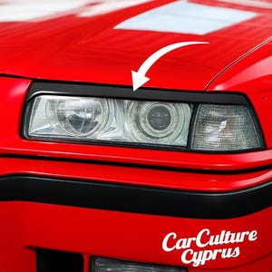 Pode incluir: Close-up da frente de um carro vermelho com acabamento preto nos faróis. Os faróis são visíveis, assim como parte do para-choques. O texto "CarCulture Cyprus" está em branco no canto inferior direito.
