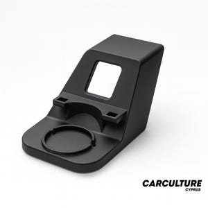 Puede incluir: Un soporte negro para teléfono de coche con portavasos y una abertura cuadrada. El soporte tiene un diseño curvo con una hendidura circular para una taza y dos pequeñas ranuras rectangulares. La marca "CARCULTURE CYPRUS" está impresa en la parte inferior derecha.