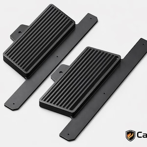 Könnte beinhalten: Zwei schwarze Autopedalabdeckungen mit geriffelter Oberfläche und rechteckiger Form. Jede Abdeckung ist an einer flachen, länglichen Basis mit Befestigungslöchern befestigt. Das CarCulture Cyprus-Logo befindet sich unten rechts.