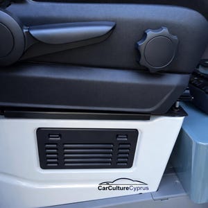 May include: A car seat detail with black leather and a white base. The seat has a black adjustment knob and a vent with horizontal slats. The text "CarCultureCyprus" is displayed on the white base.
