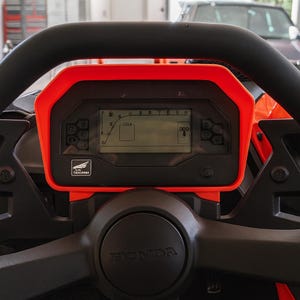 Peut inclure: Gros plan sur un volant noir avec le logo Honda. Un tableau de bord numérique avec un cadre rouge affiche des informations. Le tableau de bord comporte des boutons et un écran affichant des chiffres et des symboles. L'image est prise à l'intérieur d'un véhicule.