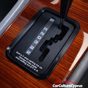 Könnte beinhalten: Nahaufnahme des Automatik-Getriebewählers eines Autos. Der schwarze Wählhebel zeigt die Gangpositionen: P, R, N, D, 3 und 2 in weißer Schrift. Der Schalthebel steht in der Position 'P'. Der Text "Shift to P when parking the car" ist sichtbar.