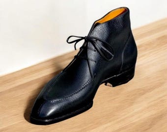 May include: A black leather ankle boot with a pointed toe and lace-up closure. The boot features a textured leather upper and a small heel. The interior lining is a bright orange color. The boot is displayed on a light brown wooden surface.