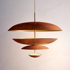 May include: A modern, tiered pendant light fixture with a copper-colored exterior and a gold-colored interior. The light has a series of overlapping, saucer-shaped shades suspended from a central rod. The fixture is designed to hang from the ceiling.