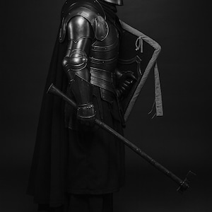May include: A grayscale image of a medieval knight in full armor, including a helmet, chest plate, and arm guards. The knight is holding a shield and a long weapon. The armor has a metallic sheen, and the knight is wearing a black cloak.