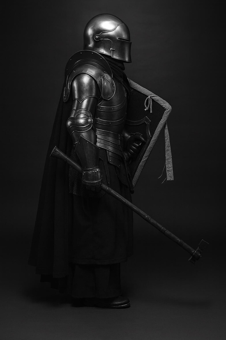 May include: A grayscale image of a medieval knight in full armor, including a helmet, chest plate, and arm guards. The knight is holding a shield and a long weapon. The armor has a metallic sheen, and the knight is wearing a black cloak.