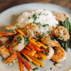 May include: A plate of cooked shrimp with rice, green beans, and colorful julienned vegetables. The shrimp are golden brown and garnished with fresh parsley. The dish is served on a light green plate.