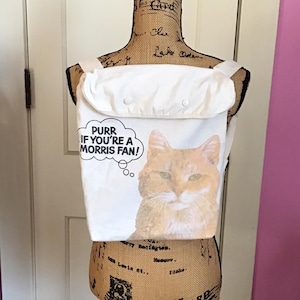 May include: White canvas backpack with a cat graphic and the text "PURR IF YOU'RE A MORRIS FAN!" printed on the front.