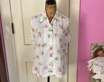May include: A white sleeveless blouse with a collared neckline and button closure. The blouse features a floral print with pink, yellow, and green flowers.
