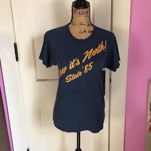 Könnte beinhalten: Ein marineblaues T-Shirt mit einer goldenen Grafik, auf der "Down it's North! State '85" steht.