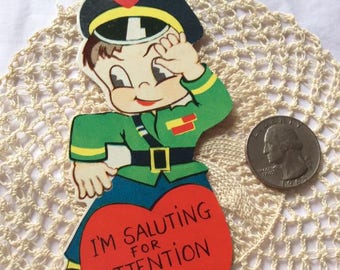 May include: Vintage Valentine's Day card featuring a cartoon soldier saluting with a red heart that says "I'm Saluting for Attention Valentine". Made in USA by Curran Co.