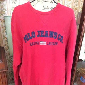 May include: Red long-sleeve sweatshirt with a navy blue embroidered logo that reads "Polo Jeans Co. Ralph Lauren" with a small American flag.