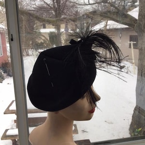 Puede incluir: Un sombrero de fieltro negro con un adorno de plumas negras. El sombrero est&aacute; en una cabeza de maniqu&iacute;.